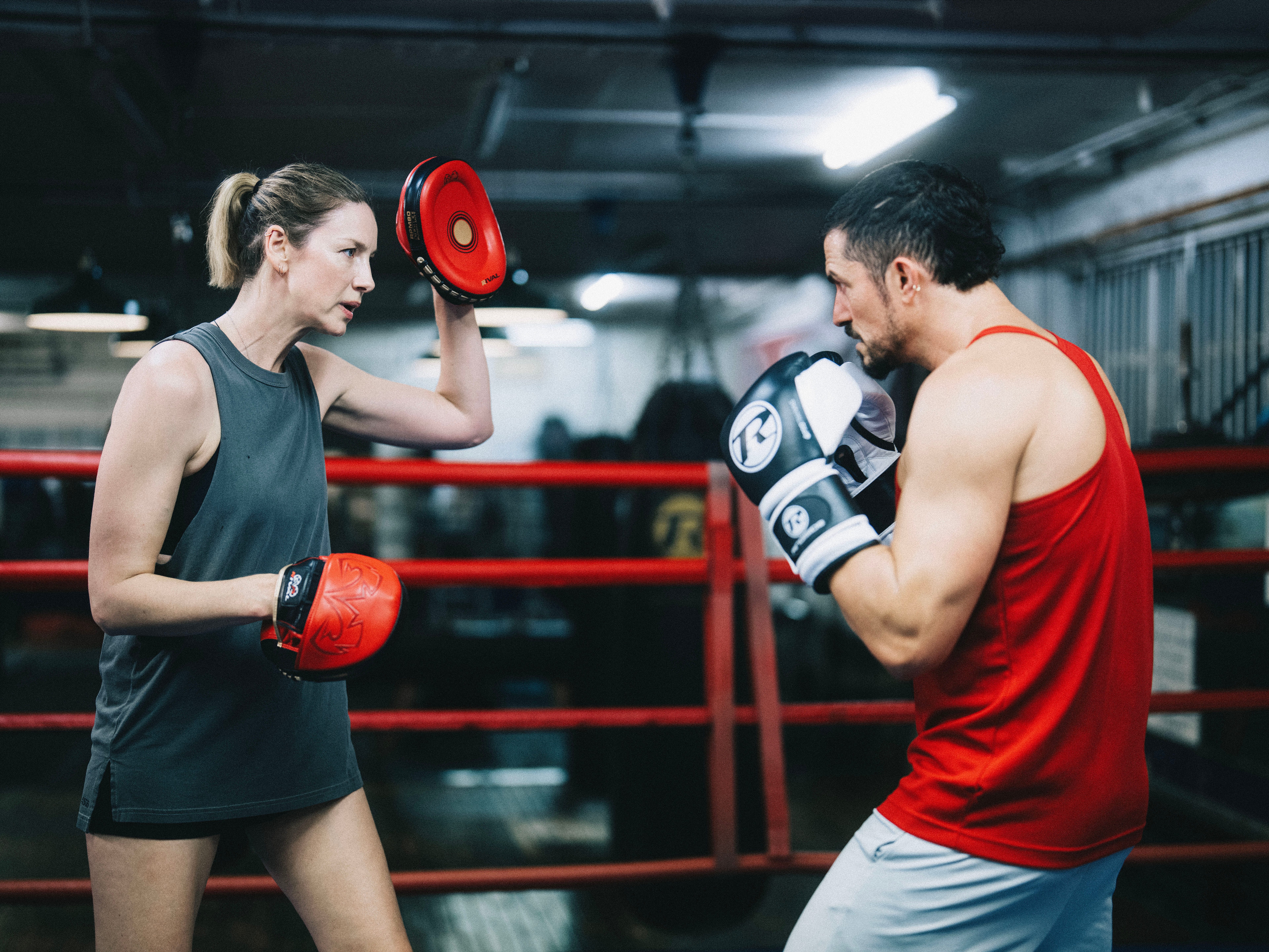 A woman holds up a bag for a man to punch.
