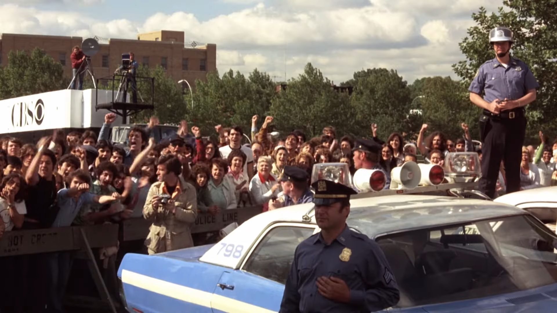 Two police officers standing in front of a crowd of people in Dog Day Afternoon.
