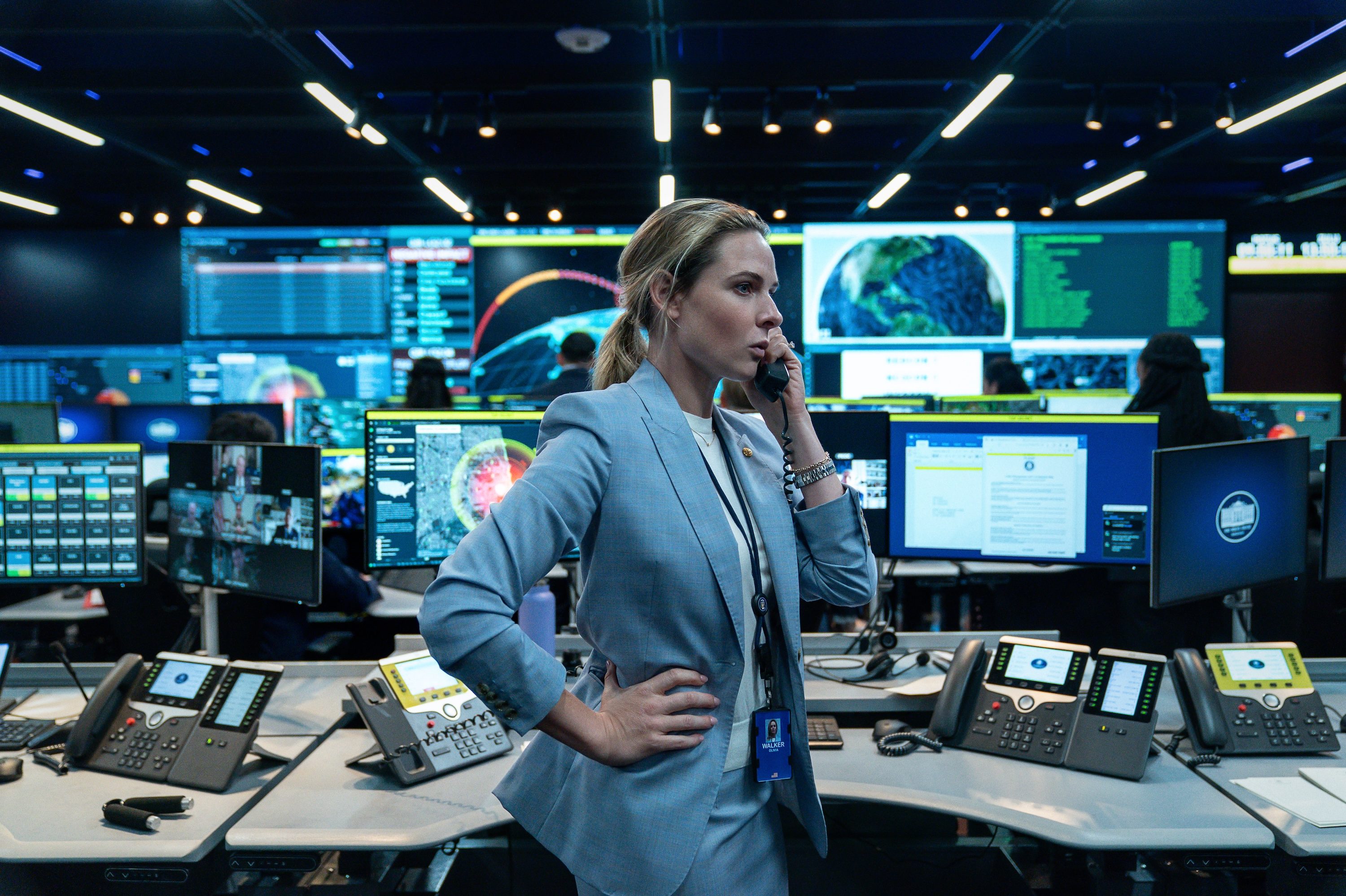 A woman holds a phone in front of computer screens.