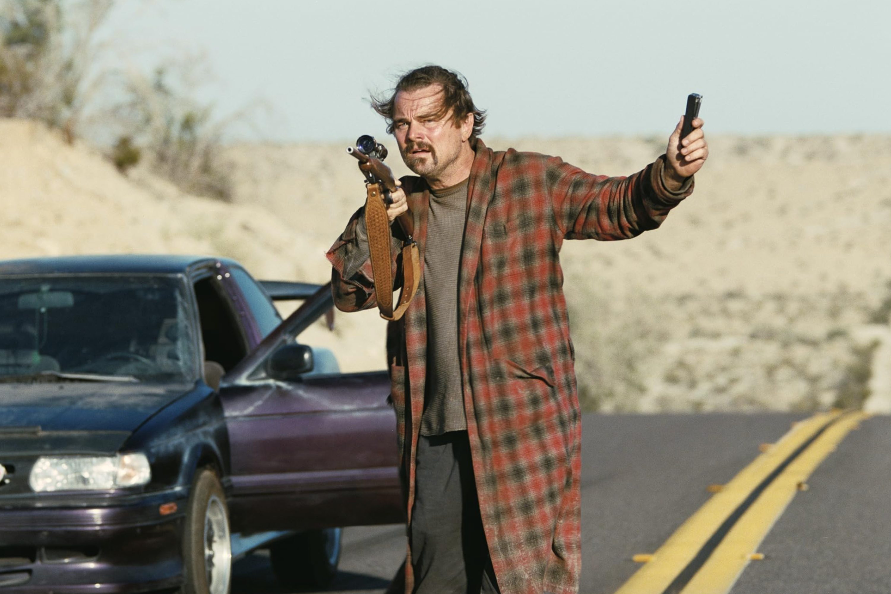 Leonardo DiCaprio points a gun and stands in One Battle After Another.