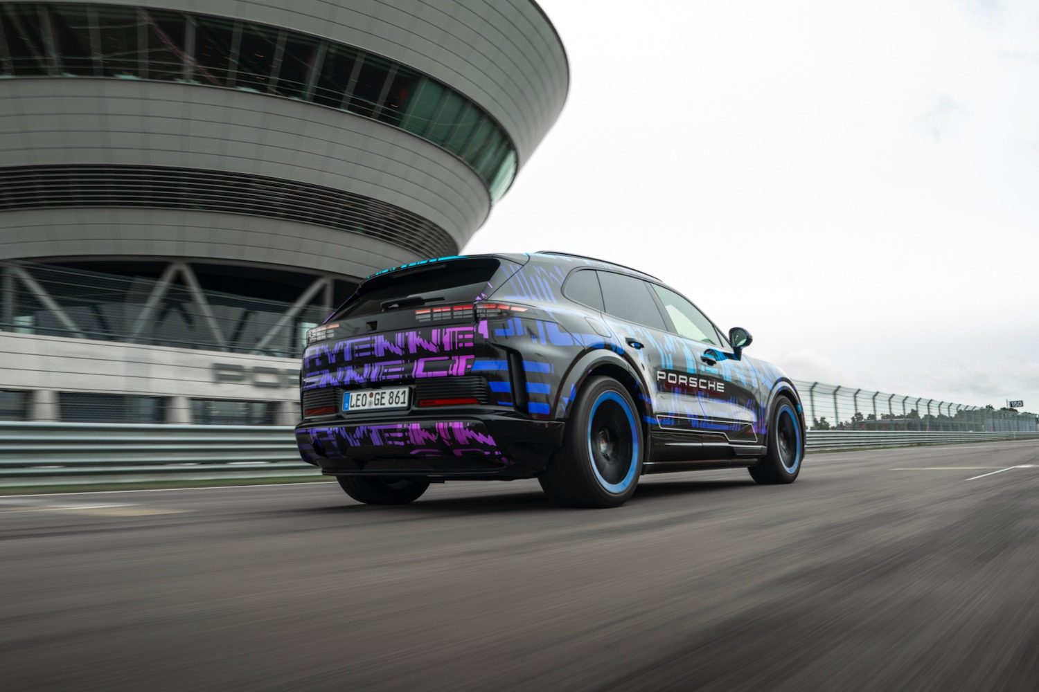 A camouflaged Porsche Cayenne Electric prototype driving on a test track.