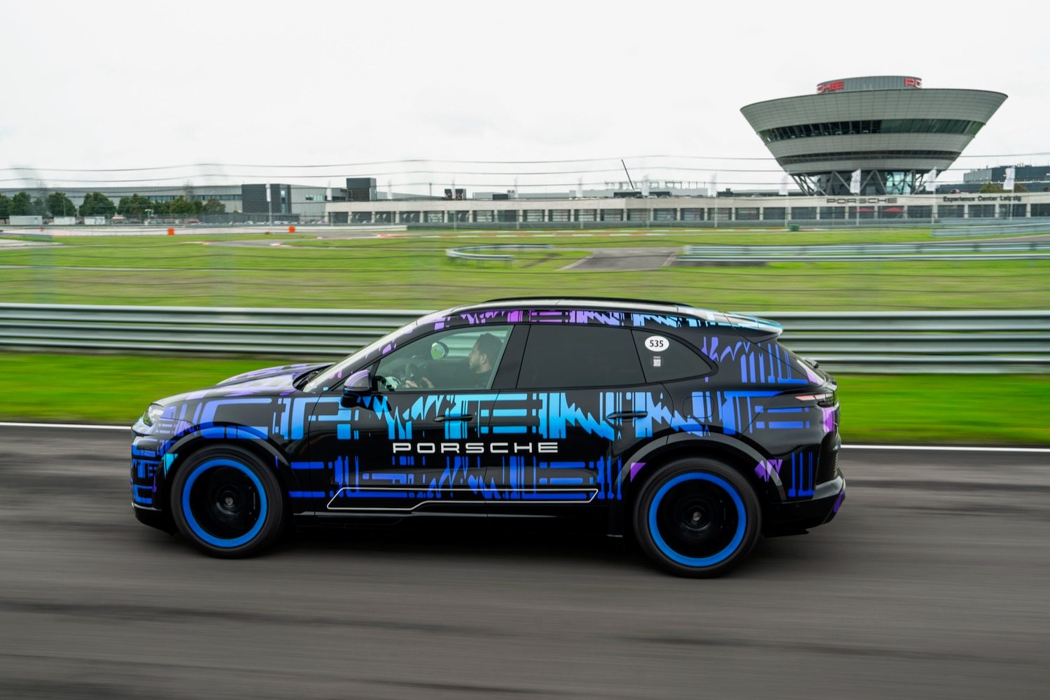 A camouflaged Porsche Cayenne Electric prototype driving on a test track.