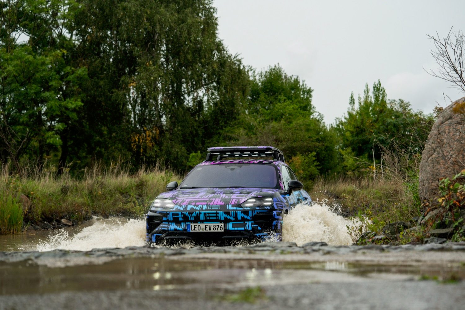 A camouflaged Porsche Cayenne Electric prototype wading through a body of water.