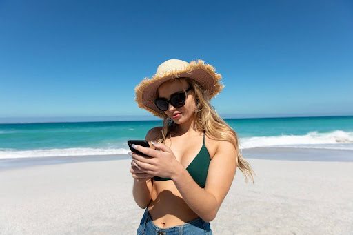 woman texting on the beach in a hat