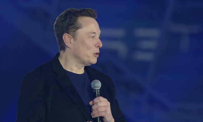 Elon Musk speaking into a microphone with a blue background