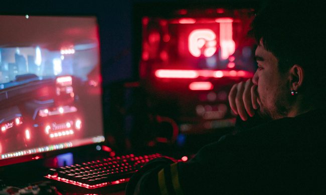 Man playing a video game on a desktop with glowing red and blue lights