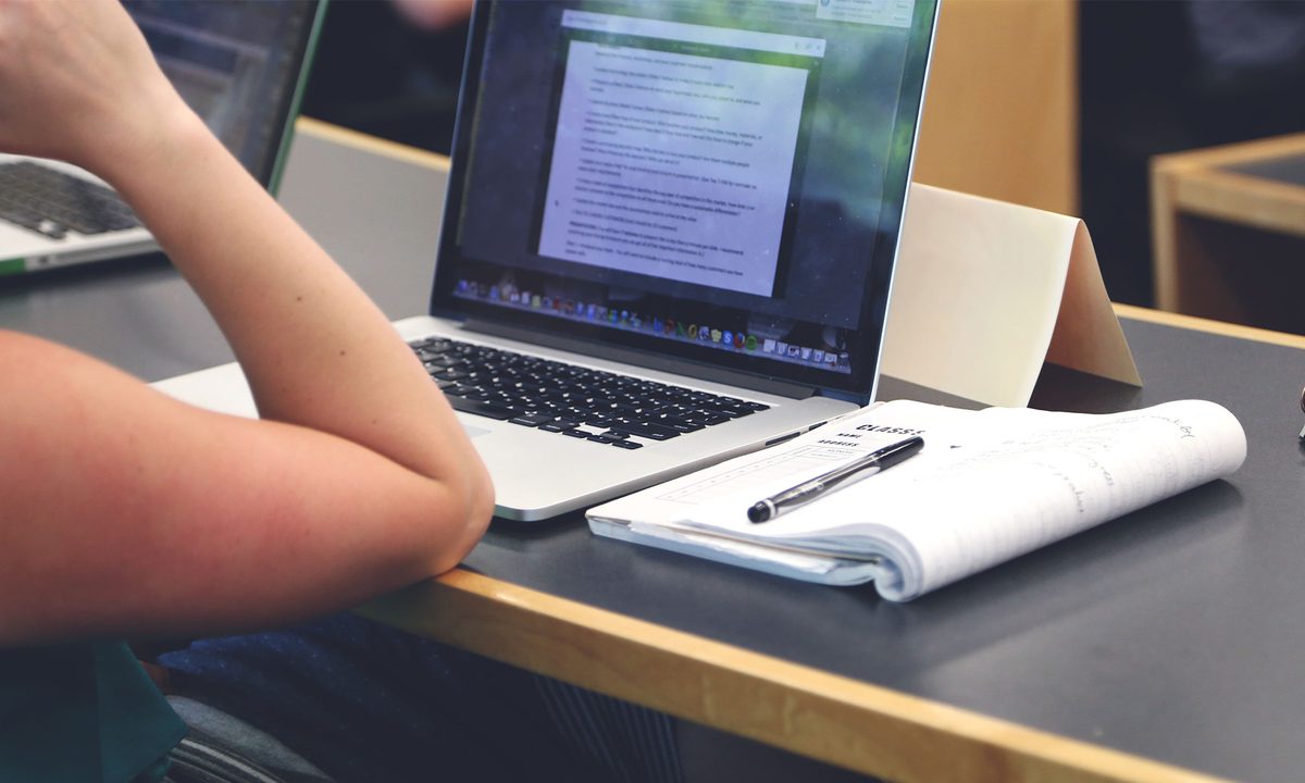 Student taking notes in classroom with laptop macbook