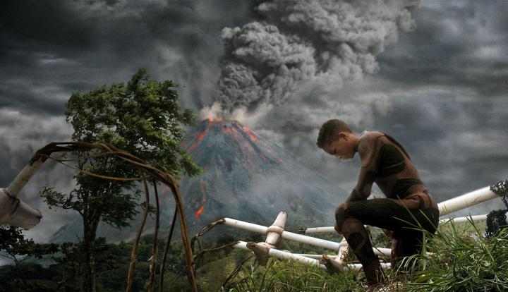 A young boy kneeling with a volcano erupting in the background in the movie After Earth.