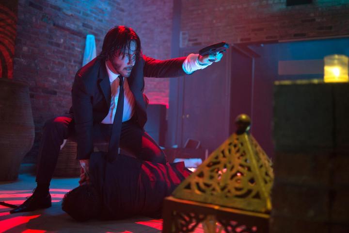 John Wick holds a gun and points it.