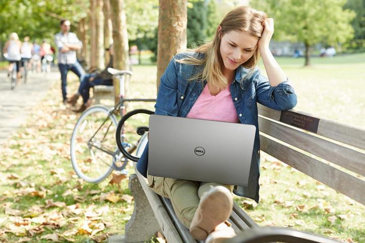 A woman sitting on a bench looking at the Dell inspiron 16 5000.