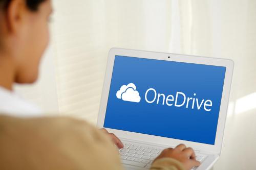 An individual using a laptop that shows the logo for Microsoft OneDrive.