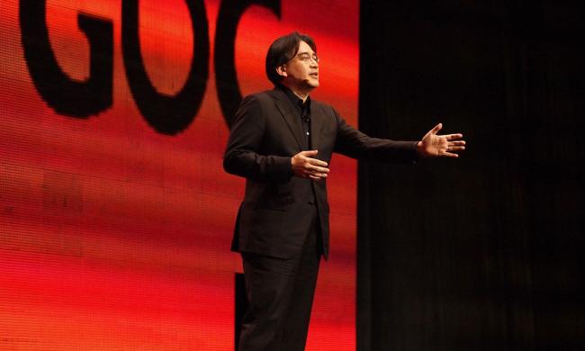 Satoru Iwata presenting at GDC in 2011 in front of a red GDC logo.