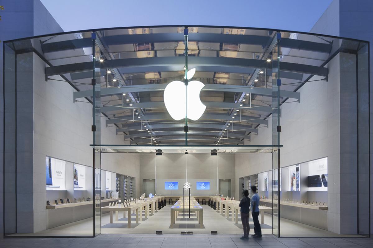 Two people look through the glass into an empty Apple store. 