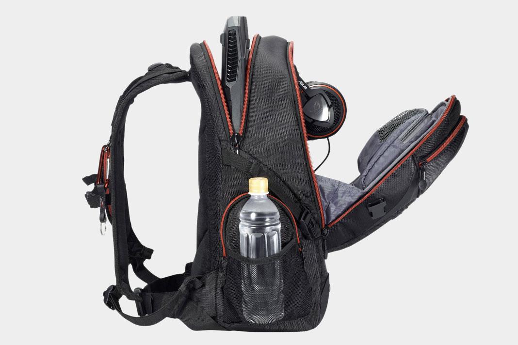 A profle view of an Asus ROG Nomad V2 backpack showing the backpack opened up and filled with tech accessories and a water bottl