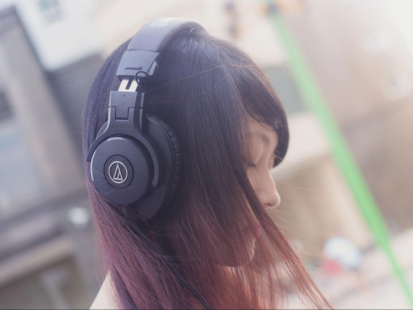 Young woman wearing the Audio-Technica ATH-M30x with city backdrop.