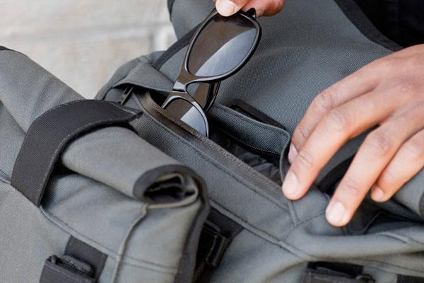 Close up shot of a person putting a pair of sunglasses into a Mission Workshop R6 Arkiv Field Pack.