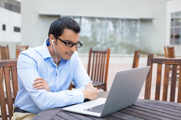 A person sitting at a table and watching something on a laptop.