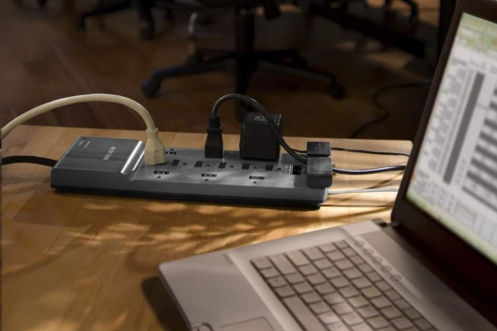 Belkin 12-Outlet surge protector on a desk next to a laptop.