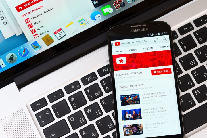 A smartphone displaying YouTube on its screen as it lays on top of a laptop's keyboard.