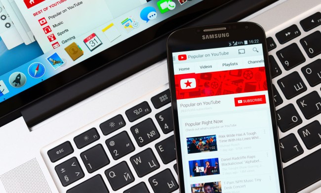 A smartphone displaying YouTube on its screen as it lays on top of a laptop's keyboard.