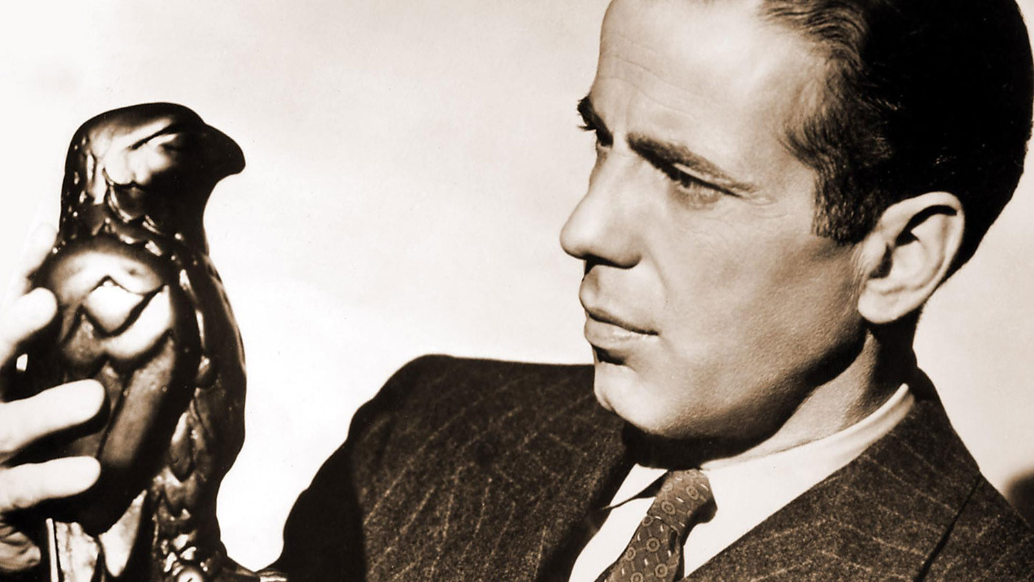 Humphrey Bogart as Sam Spade looking at the Maltese Falcon statuette.