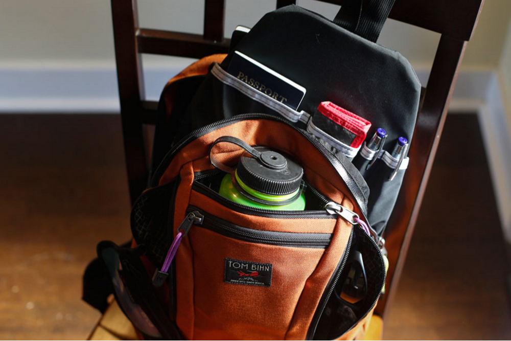 A frontal view of a Tom Bihn Synapse 19 backpack opened up and filled with various supplies like a water bottle.
