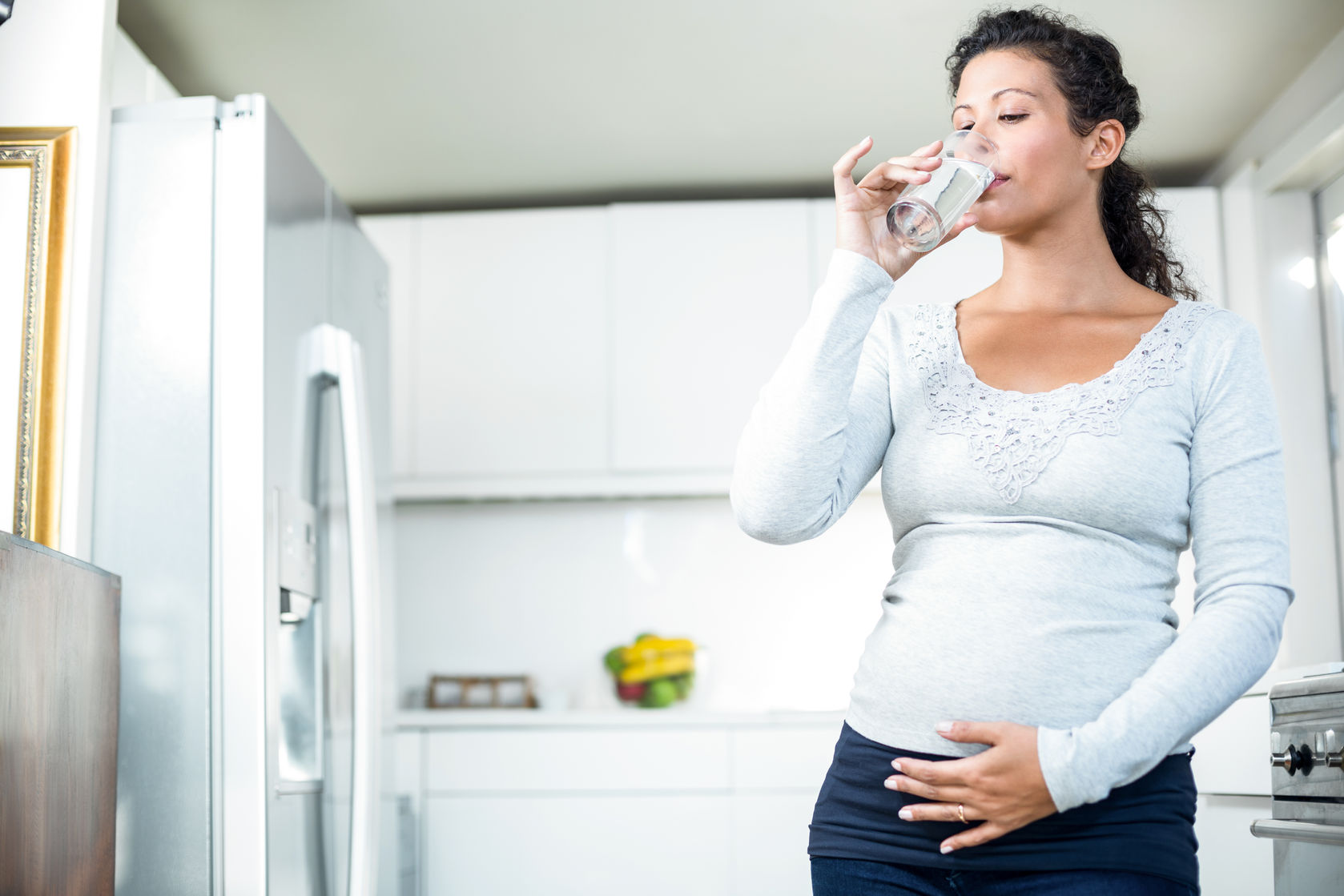 beware counterfeit refrigerator water filters pregnant woman drinking a glass of while standing in the kitchen