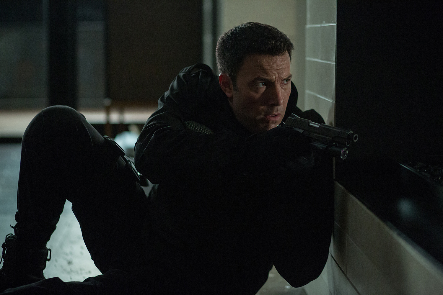 Ben Affleck crouches and holds a gun in The Accountant.
