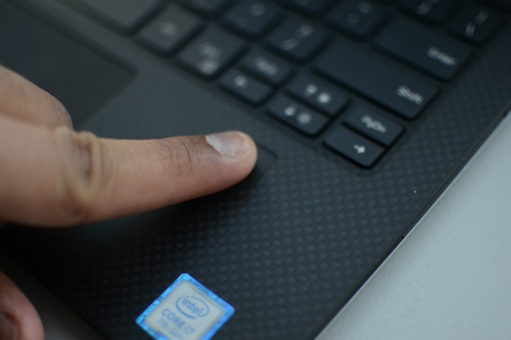 A finger pressing on a fingerprint reader on a laptop.