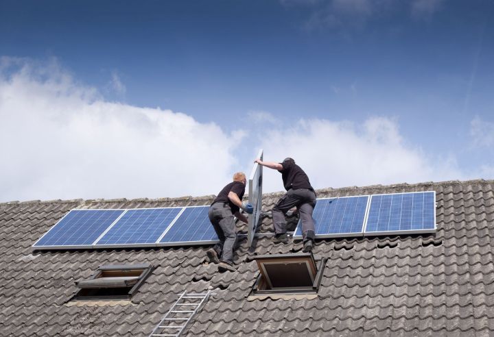 Two men installing a solar panel on a roof.