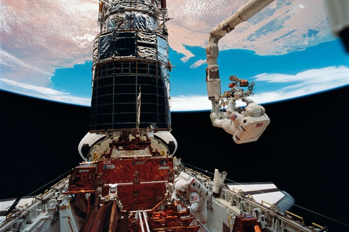 El astronauta F. Story Musgrave, anclado en el extremo del brazo del Sistema de Manipulación Remota (RMS, por sus siglas en inglés), se prepara para ser elevado a la parte superior del imponente Telescopio Espacial Hubble para instalar cubiertas protectoras en los magnetómetros. El astronauta Jeffrey A. Hoffman ayudó a Musgrave con las tareas finales de mantenimiento en el telescopio, concluyendo cinco días de actividades extravehiculares (EVA) durante la primera misión de servicio en 1990.