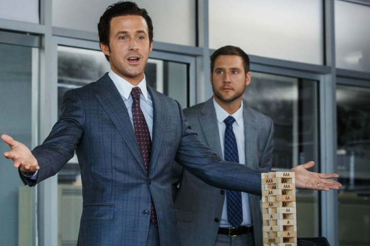 Ryan Gosling stands with his arms out by Jenga blocks in the Big Short.