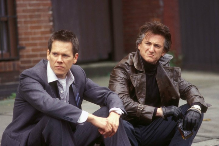 Kevin Bacon y Sean Penn sentados en una acera uno al lado del otro.