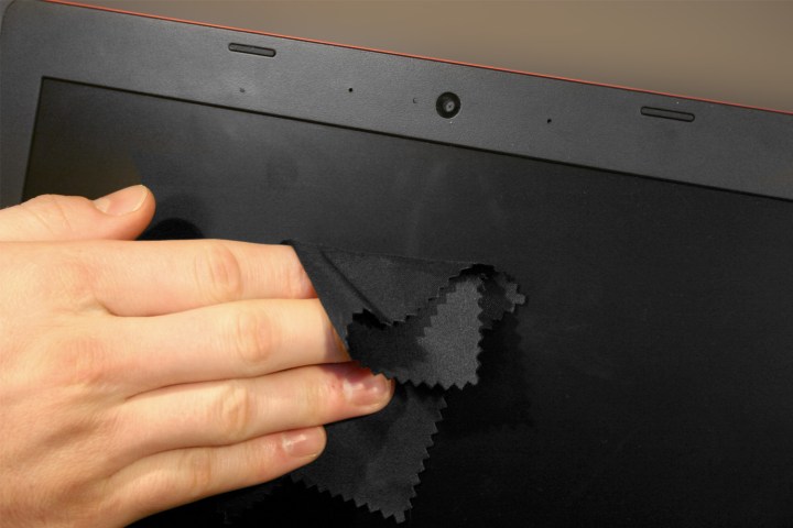 دست شخص صفحه لپ تاپ را با پارچه میکروفیبر تمیز می کند.