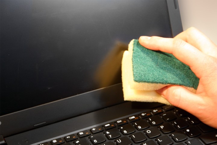 دست شخص صفحه لپ تاپ را با اسفنج تمیز می کند.