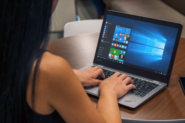 A woman sits by a desk and types on a laptop that runs Windows 10.