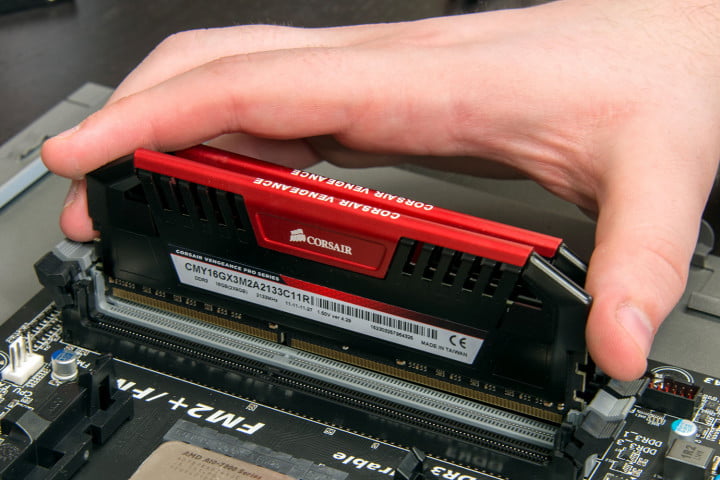 A hand inserting a stick of Corsair RAM into a desktop motherboard.