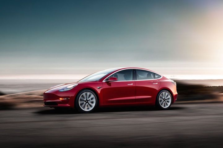 Une Tesla Model 3 rouge au crépuscule.