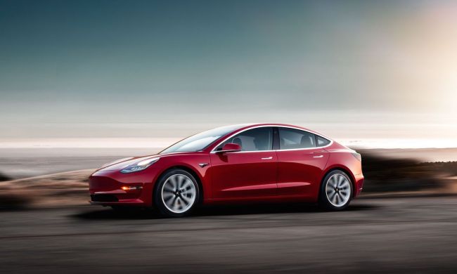 A red Tesla Model 3 at dusk.