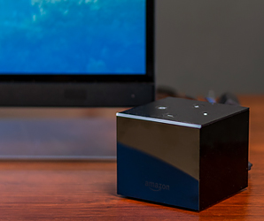 Amazon Fire TV Cube em uma mesa com uma TV ao fundo. 