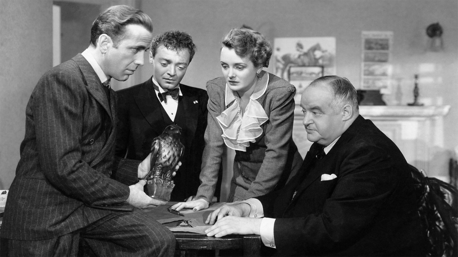 The cast of The Maltese Falcon looking at the titular statue.