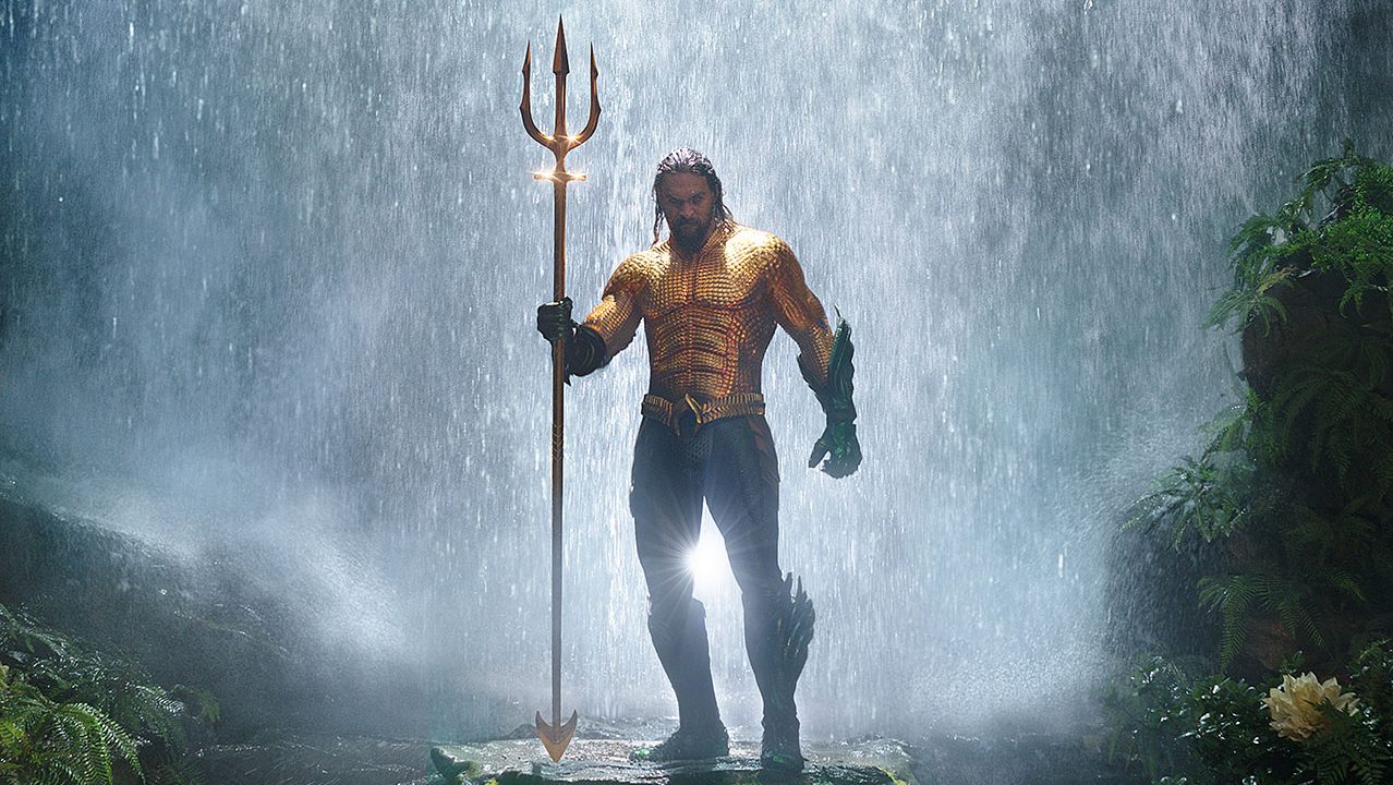 Aquaman standing in front of a waterfall holding a trident in the movie "Aquaman."