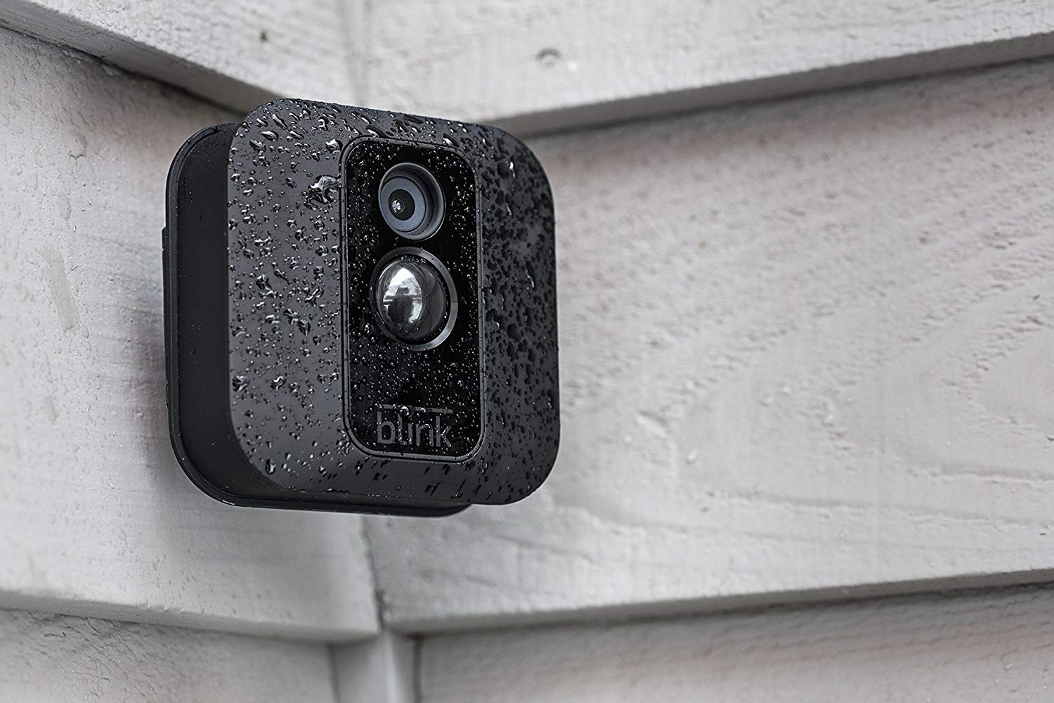 A Blink security camera covered in raindrops mounted in an exterior corner of a house.