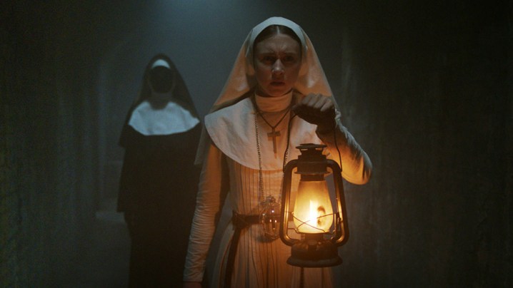 Taissa Farmiga as Sister Irene holding a lantern while Valak the demon nun stands behind her in The Nun.