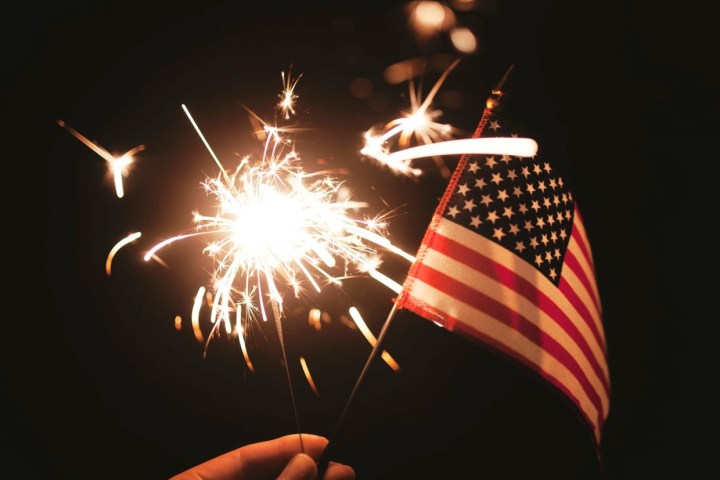 Sebuah tangan memegang bendera Amerika dengan kembang api kembang api.