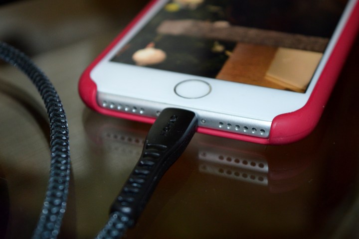 Braided lightning cable plugged into an older iPhone in a red shell case.