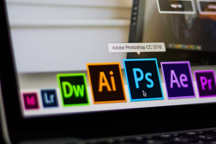 نمای نزدیک از نماد برنامه Adobe Photoshop انتخاب شده در میان سایر برنامه های Adobe بر روی صفحه نمایش لپ تاپ.