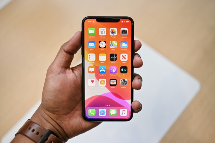 A hand holds an Apple iPhone 11 Pro Max showing apps on the screen.