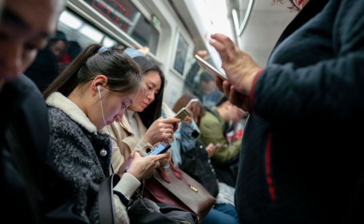 people immersed in using their smartphones on a subway train.