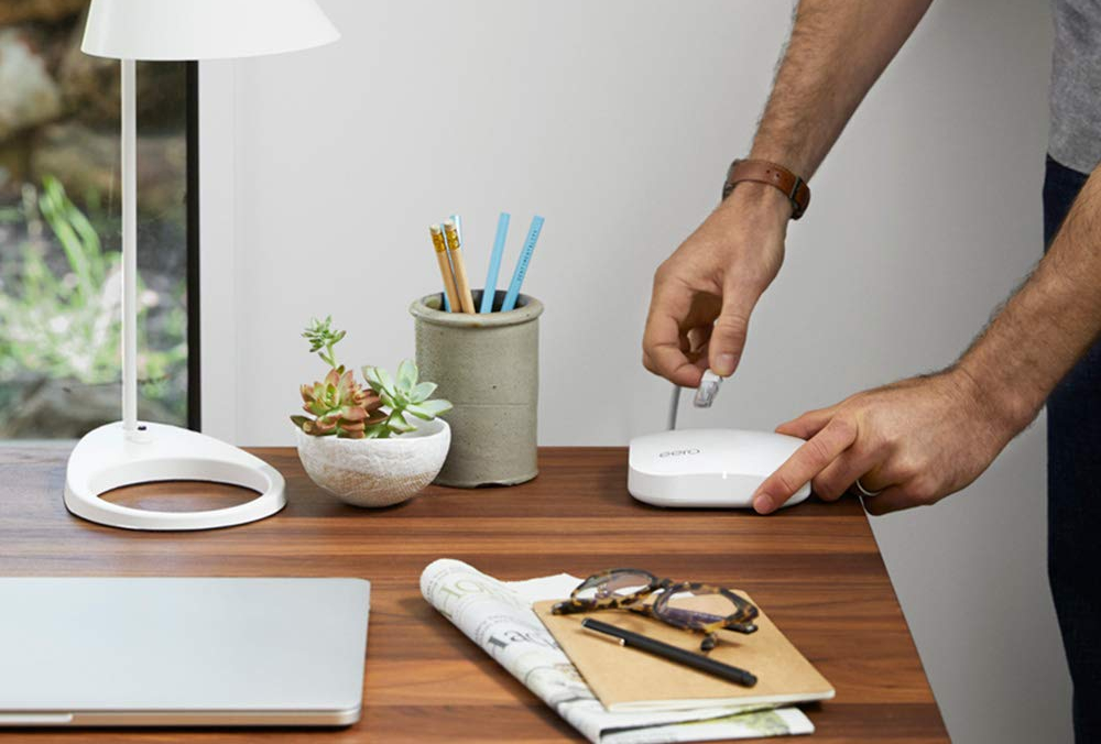 A pair of hands working with a Eero Pro Mesh WiFi router-extender at a wooden desk.